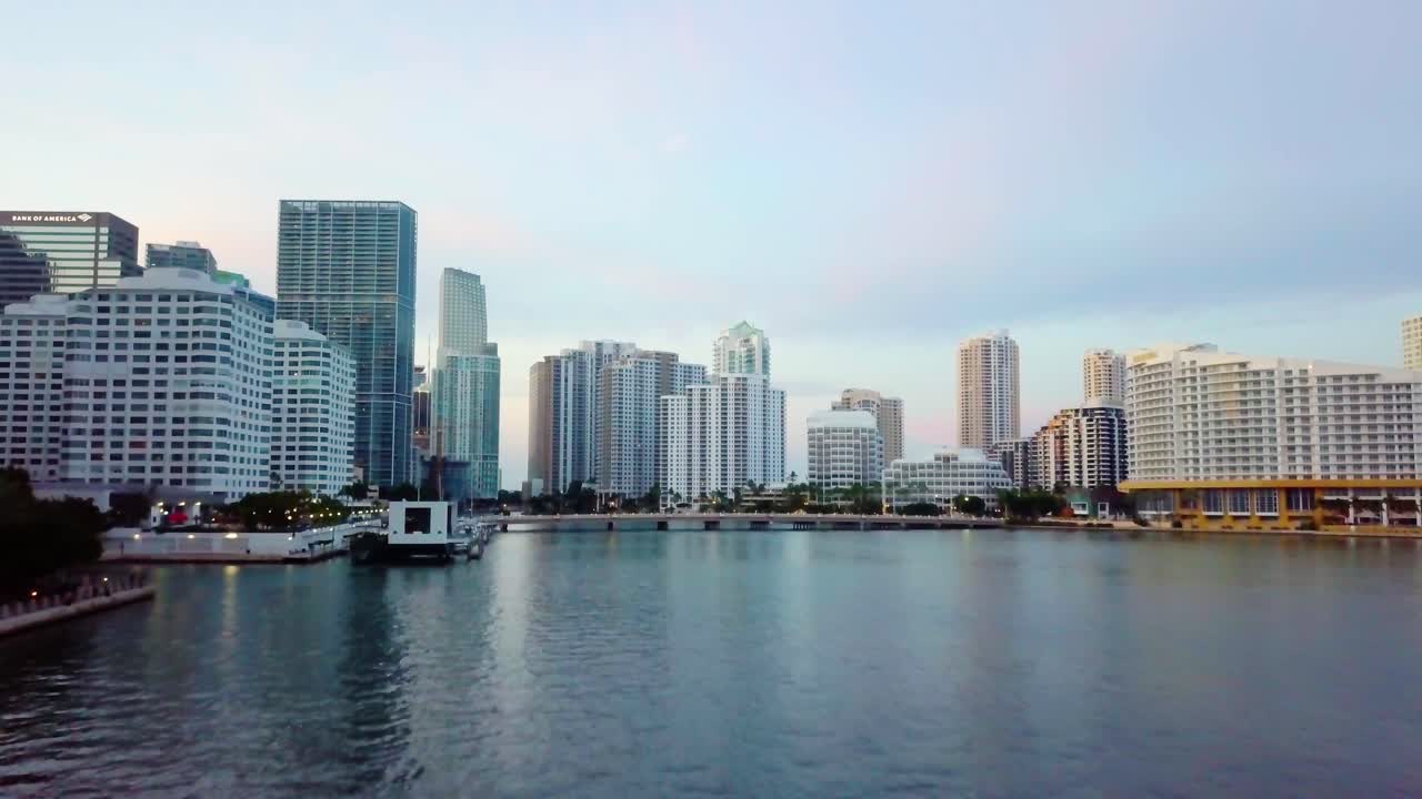 Aerial view low over the sea towards skyscrapers and the Brickell key bridge, during sunrise, in Miami, Florida, USA - dolly, drone shot