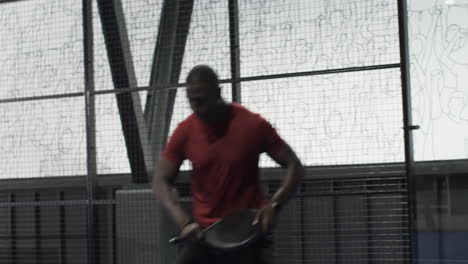 man playing padel tennis, focusing on hitting ball against glass wall, at indoor court