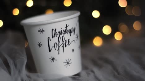 christmas decor coffee paper cup with cozy fairy lights, closeup macro