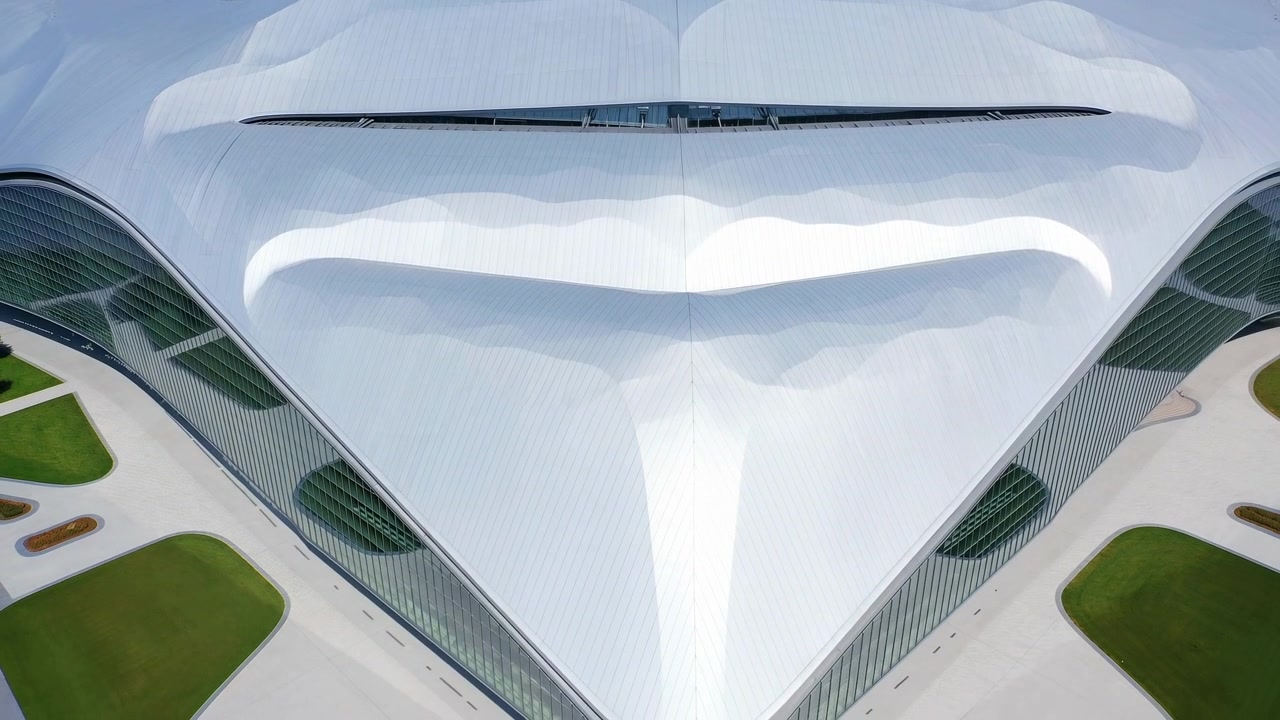 Vista aerea di un complesso futuristico con tetto bianco che mostra un'ampia tettoia curva e una superficie liscia e riflettente.