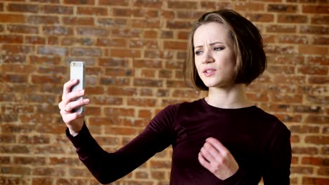 Young beautiful girl has video call on her smartphone, communication concept, brick background