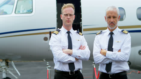 two male pilots standing with arms crossed on a runway 4k