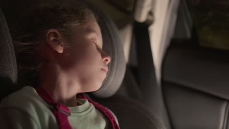 a close view of a child peacefully sleeping in a car seat at night, with the soft glow of streetlights and passing cars visible through the window, resting comfortably