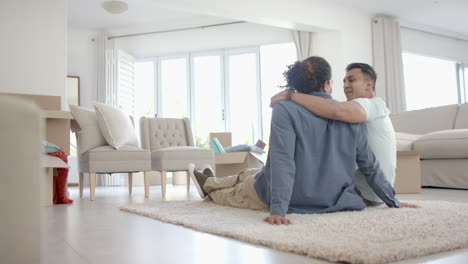 Happy-diverse-gay-male-couple-in-new-home,-sitting-on-rug-in-living-room,-copy-space,-slow-motion