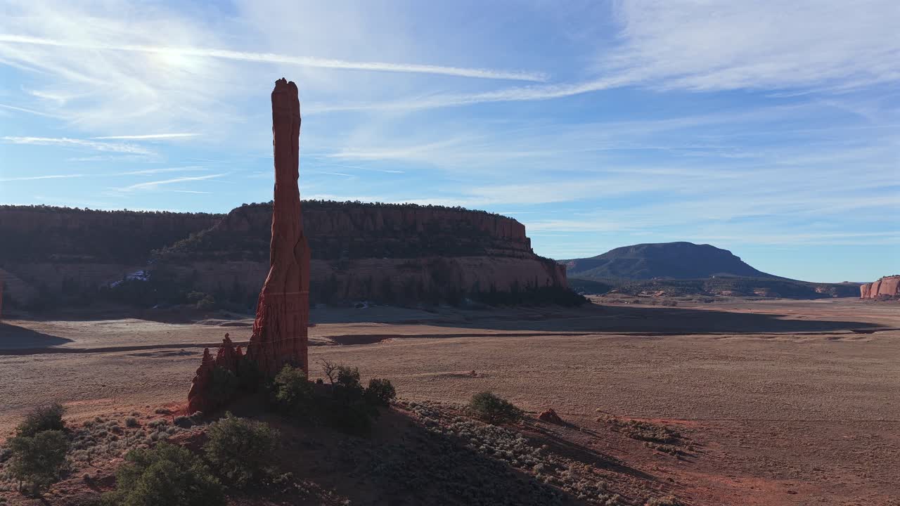 Una ripresa con drone cattura un lento e drammatico movimento in avanti dietro una solitaria guglia di roccia rossa, incorniciando uno sfondo di canyon epico. Sottolinea le aspre texture geologiche e la maestosa grandezza di un deserto remoto.