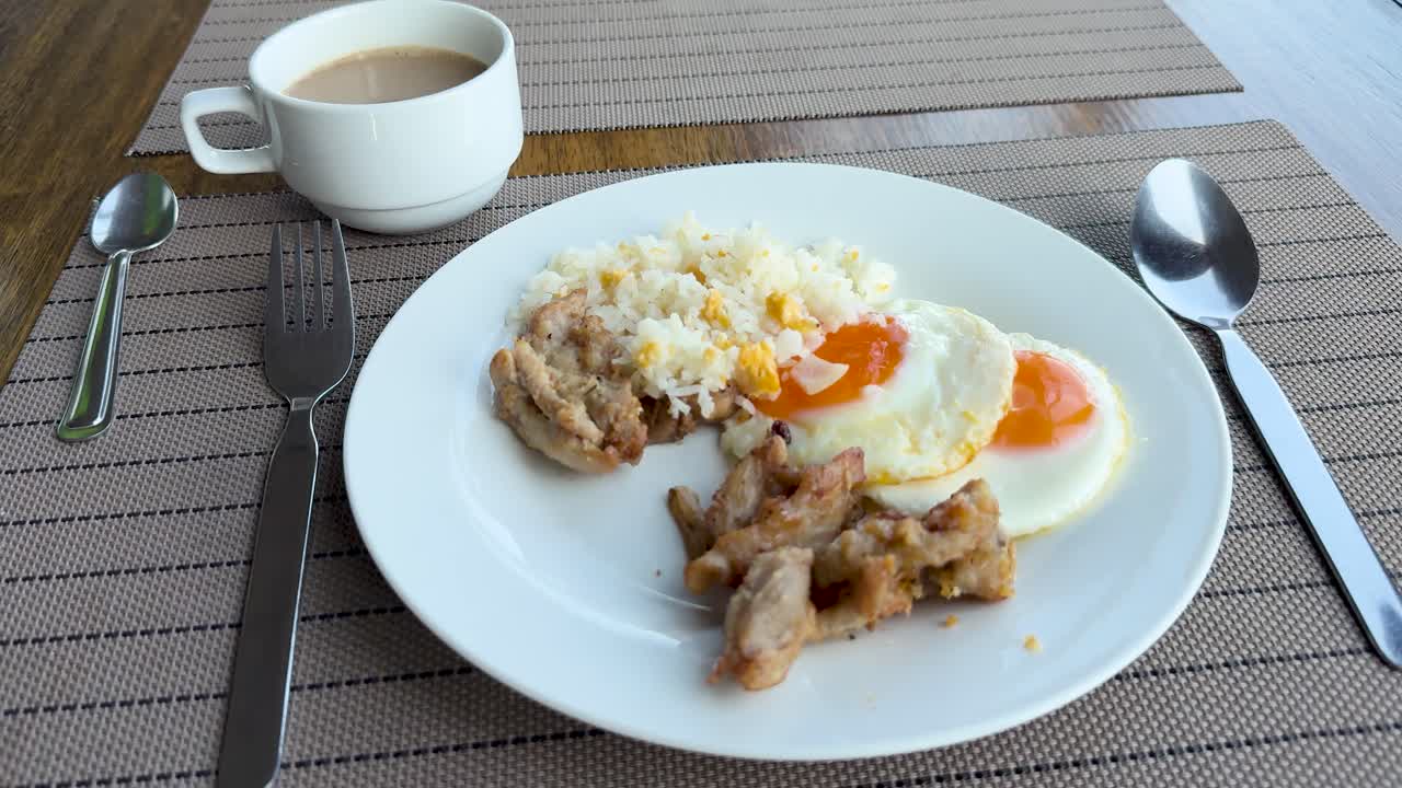 Plate of fried rice, eggs, chicken, and coffee on sunlit patio table, static camera view
