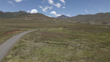 Low-aerial-follows-vehicle-driving-on-mountainous-high-plateau-meadow