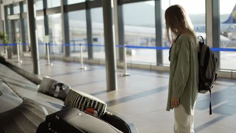 mujer de viaje esperando en el aeropuerto junto a las cintas transportadoras de equipaje