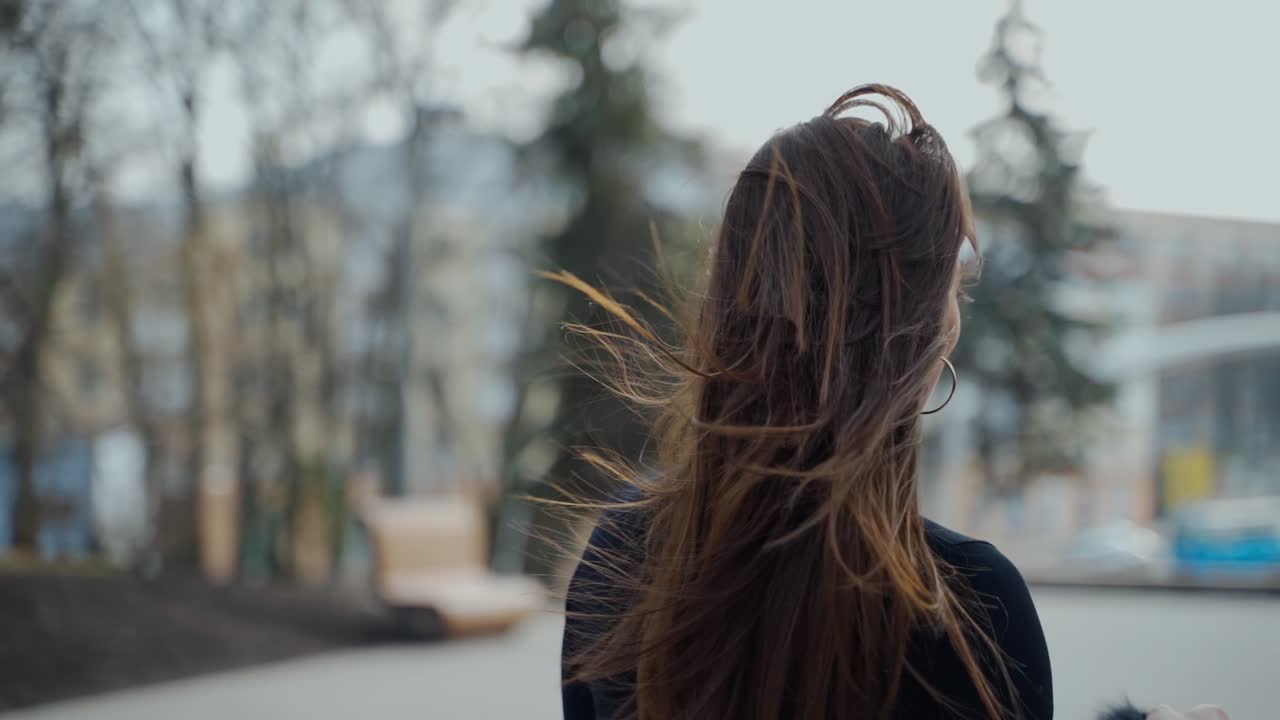 Happy girl turning around in the park. Attractive young lady with long hair in black sweater looking on camera and smiling in the street of a city. Slow motion.