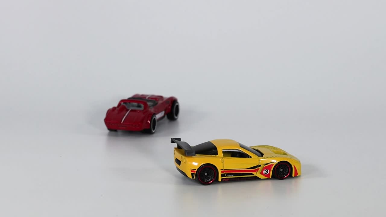 A red and yellow toy car move side by side on a smooth surface.