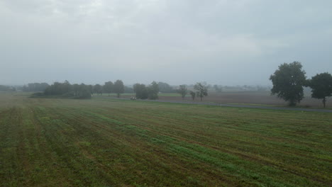 Fog-Over-Lush-Green-Fields-And-Trees-In-The-Town-Of-Lubawa-In-Poland-With-Cars-Driving-On-The-Road-On-A-Cloudy-Day