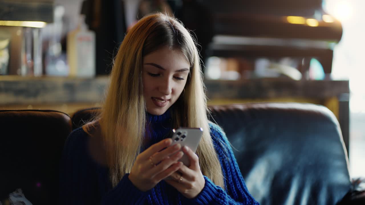A beautiful young girl sits in cafe and uses a mobile phone to scroll through social networks and send messages