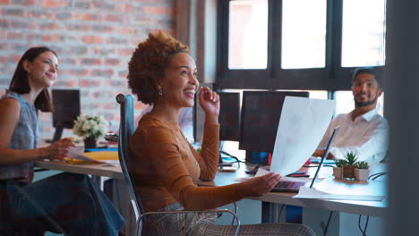 businesswoman working on laptop at desk in busy multi-cultural office