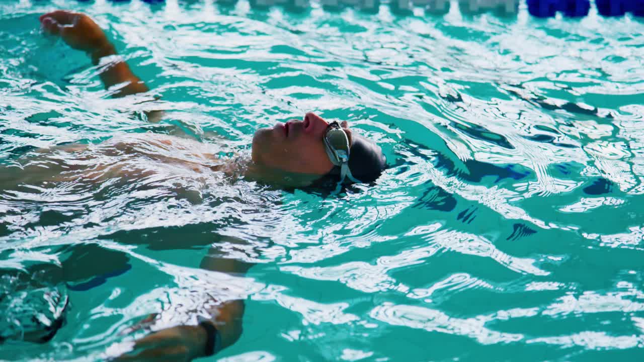A swimmer floats calmly on the surface of the pool, showcasing tranquility and relaxation amidst the shimmering aquatic environment during a moment of rest