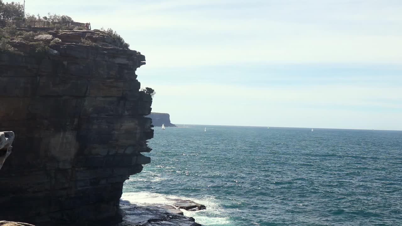 Sheer cliff looms against the vast ocean as waves splash over the rocks