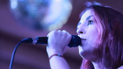 beautiful girl with microphone singing on a concert with disco spotlights on the background