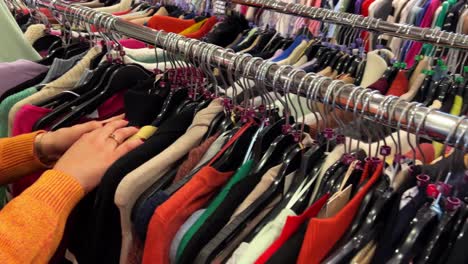 hands of woman browsing through fast fashion store clothing rack