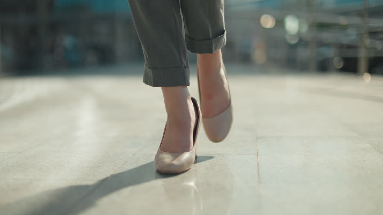 Close up leg view of elegant lady walking confidently in nude high heels on smooth polished surface with soft sunlight and blurred urban background