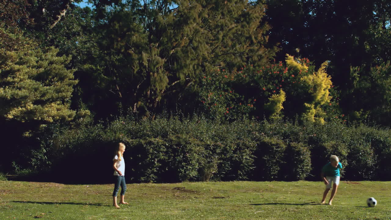 Brother and sister playing football together in a park