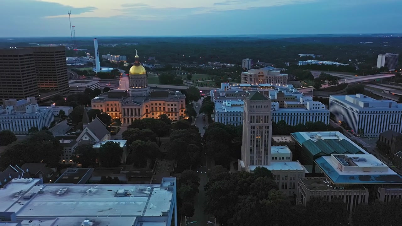 Hovedgaden i Atlantas centrum oplyst i skumringen. Luftoptagelse, der nærmer sig Georgia State Capital med gylden kuppel. Flyvning over hustage og kontorbygninger i byen. Fugleperspektiv, USA.