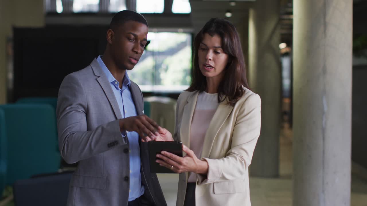 Diverse businessman and businesswoman using tablet in modern office