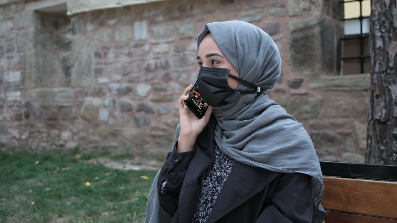 마스크를 쓴 무슬림 여성이 전화를 걸고 있습니다.