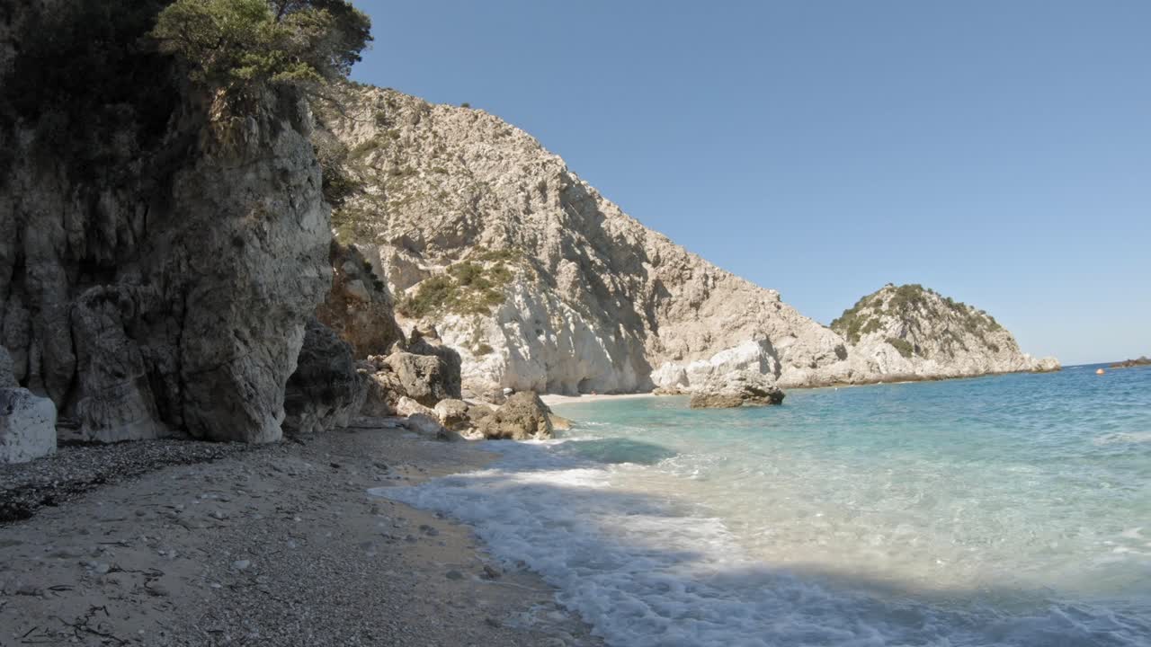 Clear waves rolling over the rocky beach by the mountain shoreline of Kefalonia