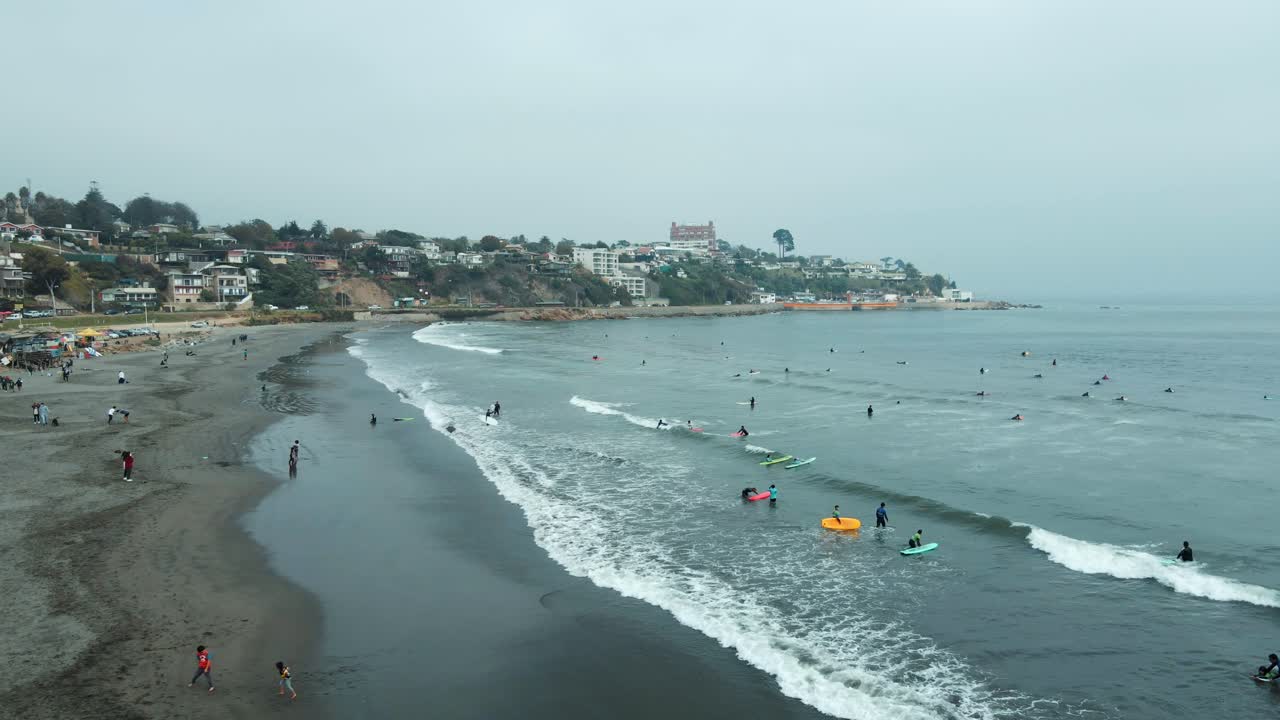 órbita aérea de personas nadando y surfeando en el mar cerca de la orilla de arena en la playa de la boca, barrio de la ladera de concon en el fondo, chile