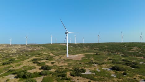 Toma-Aérea-De-Una-Plataforma-Que-Pasa-Junto-A-Una-Turbina-Eólica-Y-Revela-Un-Gran-Parque-Eólico