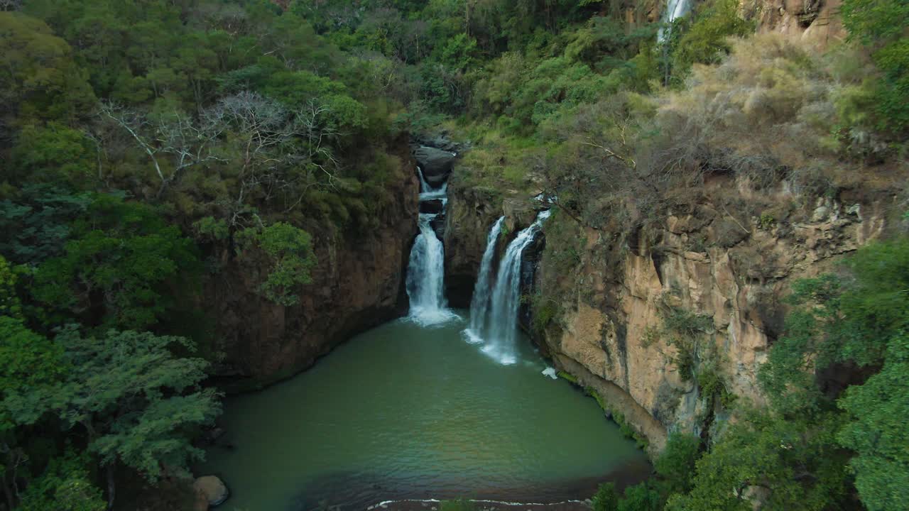 Three waterfalls cascade into a green natural pool surrounded by cliffs and dense forest, doll in drone view at Turbinas Santa Cruz, Mexico