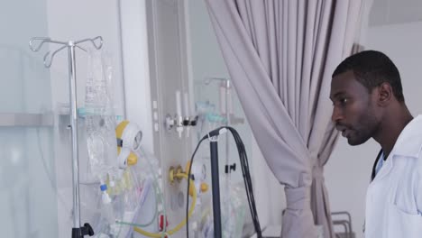 african american male doctor checking drip in hospital room, slow motion