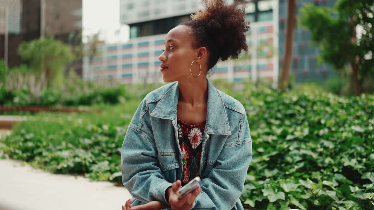 Donna con giacca di jeans che usa il cellulare in un parco urbano