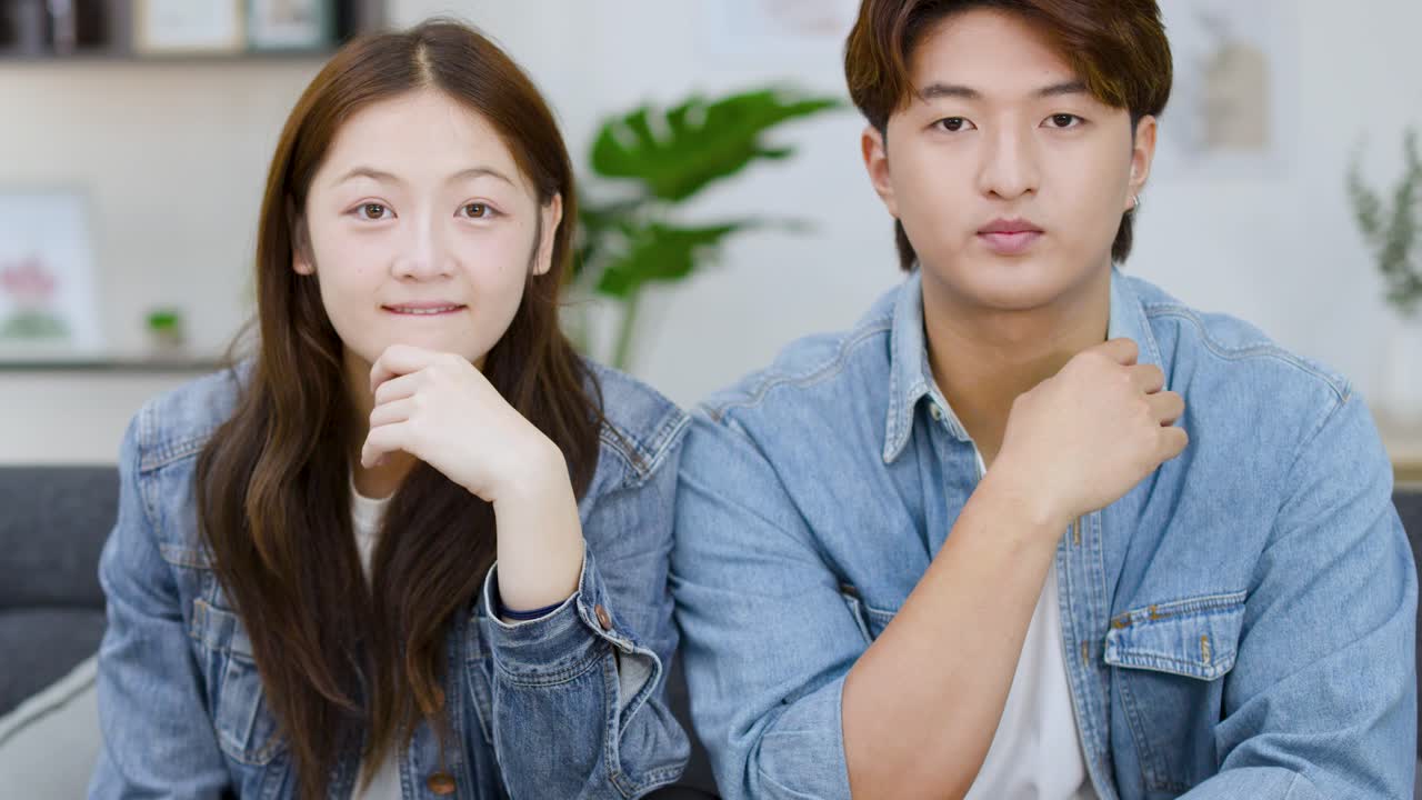 若いアジア人の男女がソファに並んで座り、テレビ番組にリアクションしている。