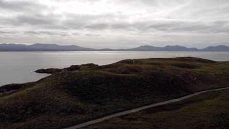 Aerial-view-Ynys-Llanddwyn-island-Anglesey-coastal-walking-trail-with-Snowdonia-mountains-across-the-Irish-sea-dolly-left-shot