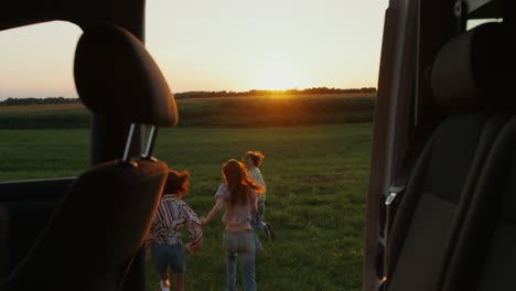 friends running in a field at sunset from car window