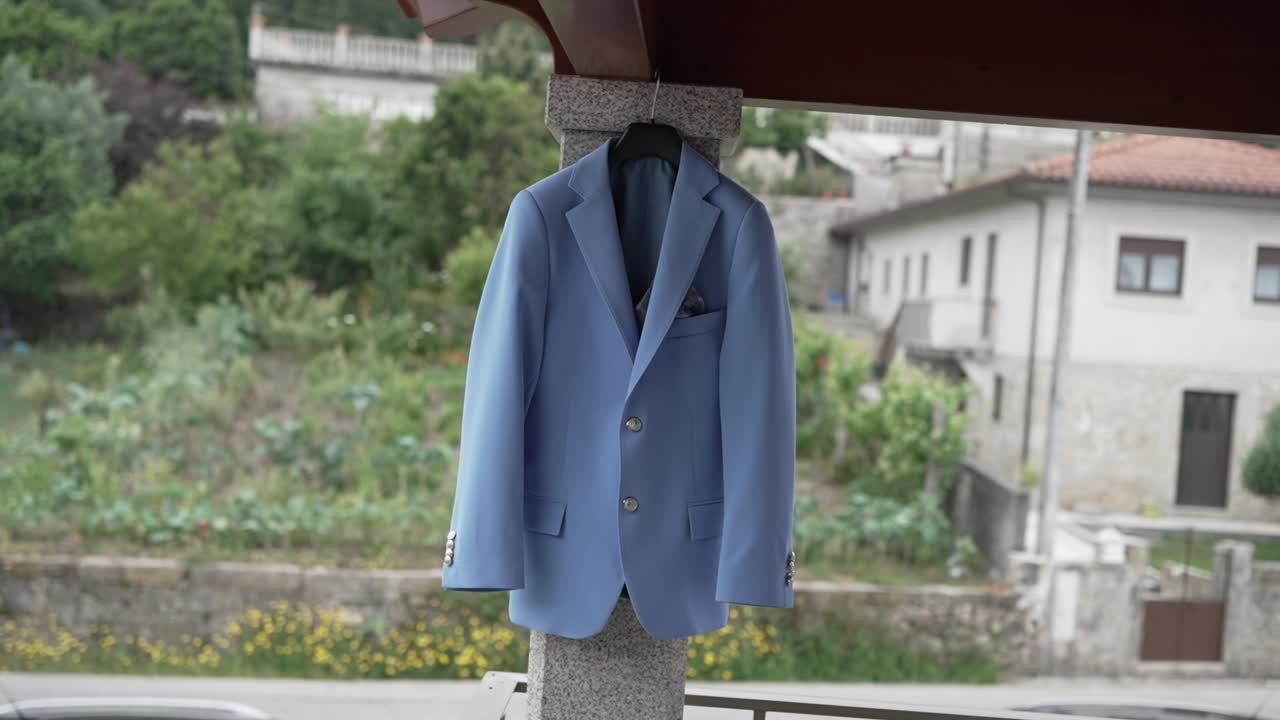 Light blue groom suit on a hanger outdoors with a rustic village backdrop