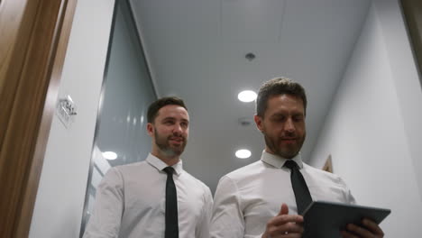 two employees talking business researching tablet device in office hallway.