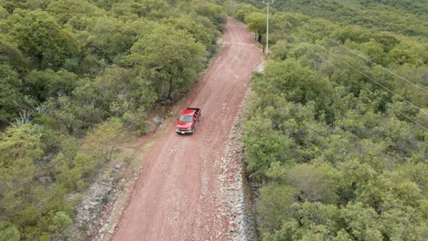 Vista-Aérea-De-Una-Camioneta-Roja-Conduciendo-Por-Un-Camino-Fangoso-En-Un-Bosque-De-Montaña,-Tiro-De-Seguimiento