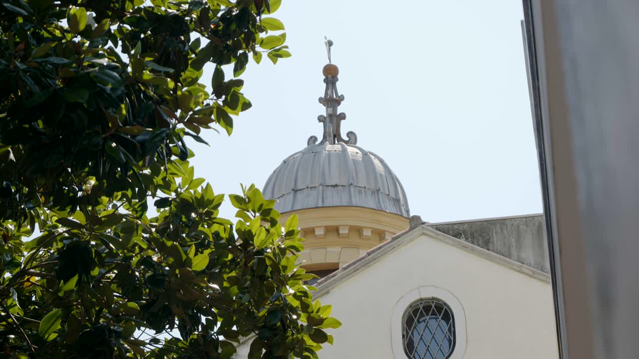 Campanile della chiesa visto attraverso foglie verdi in una giornata di sole in un paesino.