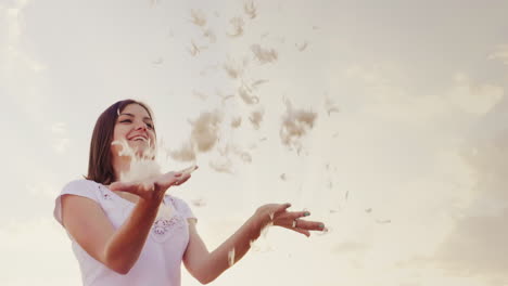 a young woman is playing with a gentle light down feathers fall into her hands