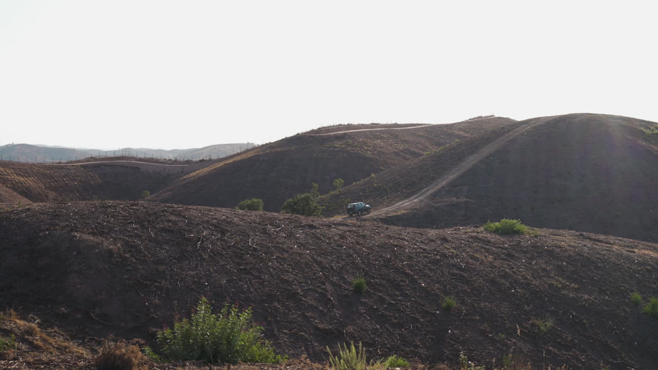 vehículo todoterreno estacionado en una colina árida, rodeado de un paisaje áspero - toma de diapositiva ancha de paralaje