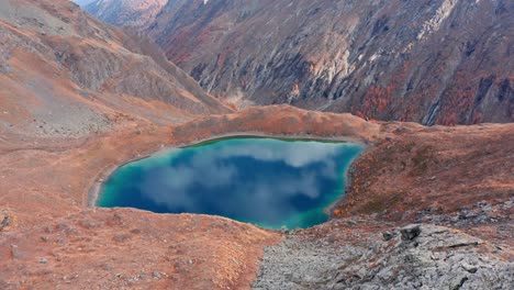 Mountain-lake-nestled-in-autumnal-valley,-vibrant-colors-reflecting-in-water,-serene-landscape