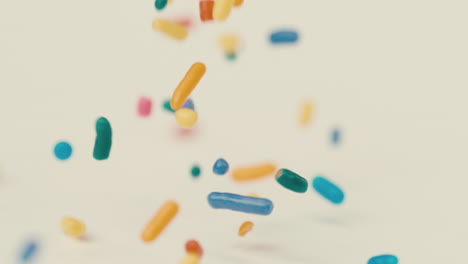 multicolor rainbow sprinkles land on white table and bounce in all directions in slow motion