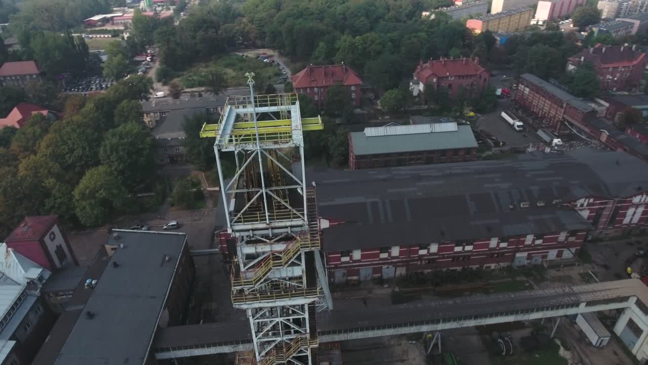 Dynamic drone shot of a tall mine shaft in a large mine, surrounded by trees and buildings in Silesia on a cloudy day, in 4K resolution