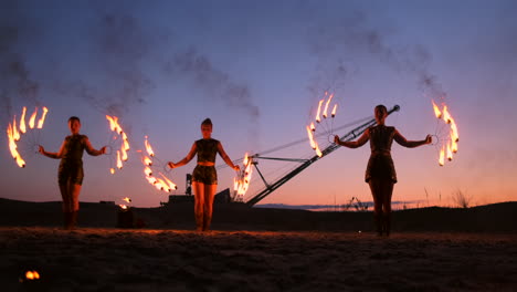 professional artists show a fire show at a summer festival on the sand in slow motion. fourth person acrobats from circus work with fire at night on the beach