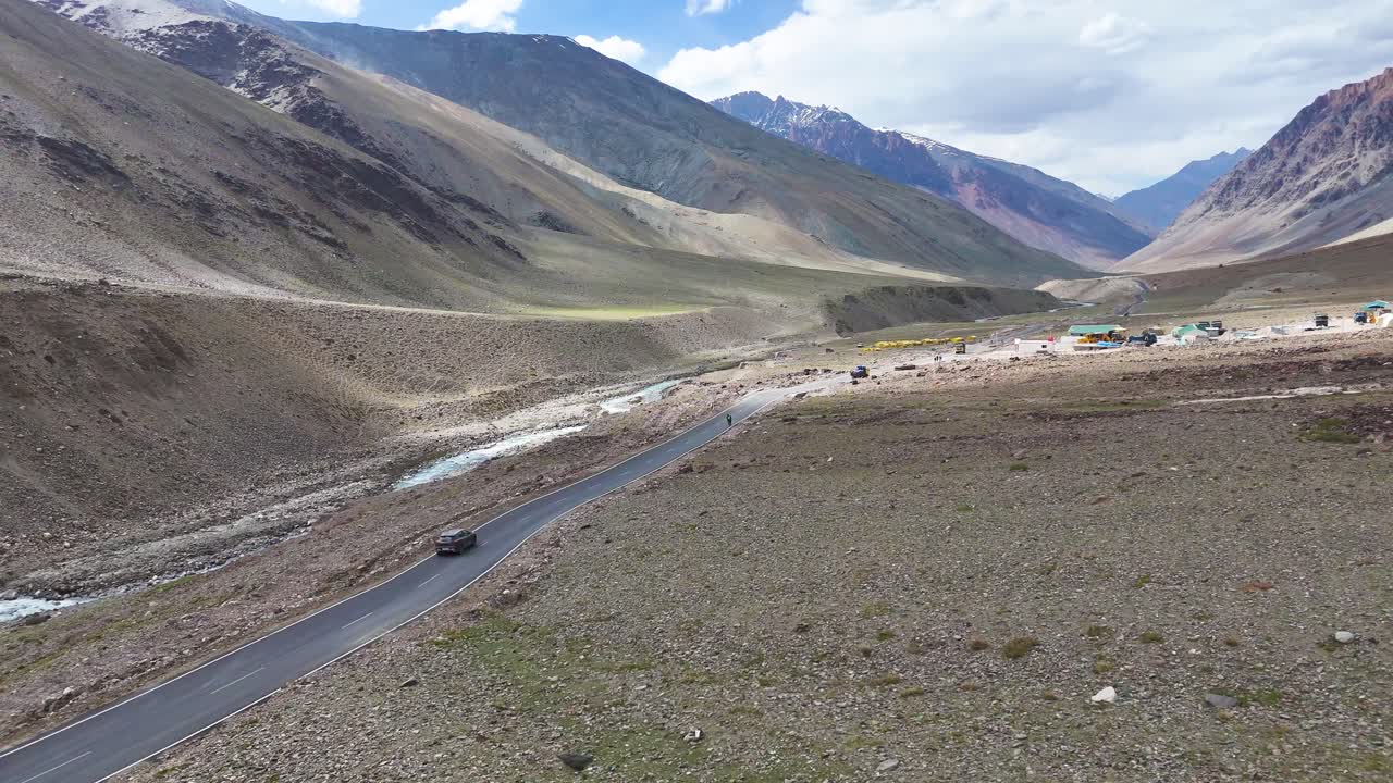Aerial drone shot capturing a solitary car on a long straight road crossing the high-altitude Ladakh region.