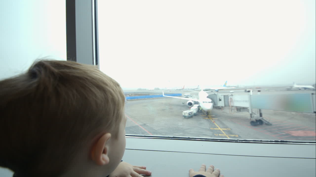 Little boy looking out window and pointing at plane