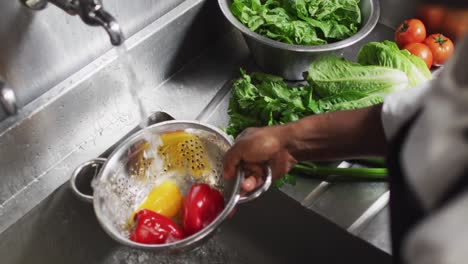 african american female chef washing vegetables in colander in restaurant kitchen