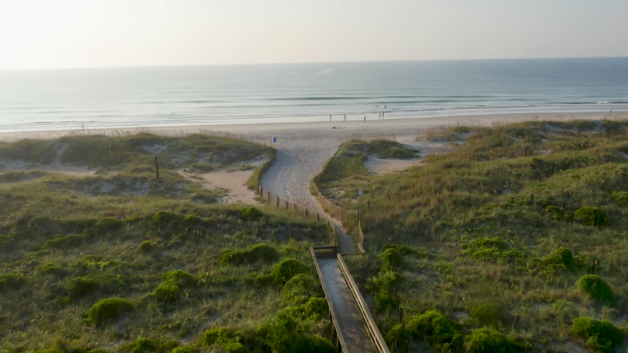 vista de 4k de dunas verdes y acceso a la playa de madera que conduce a una playa al amanecer con gente saliendo a caminar