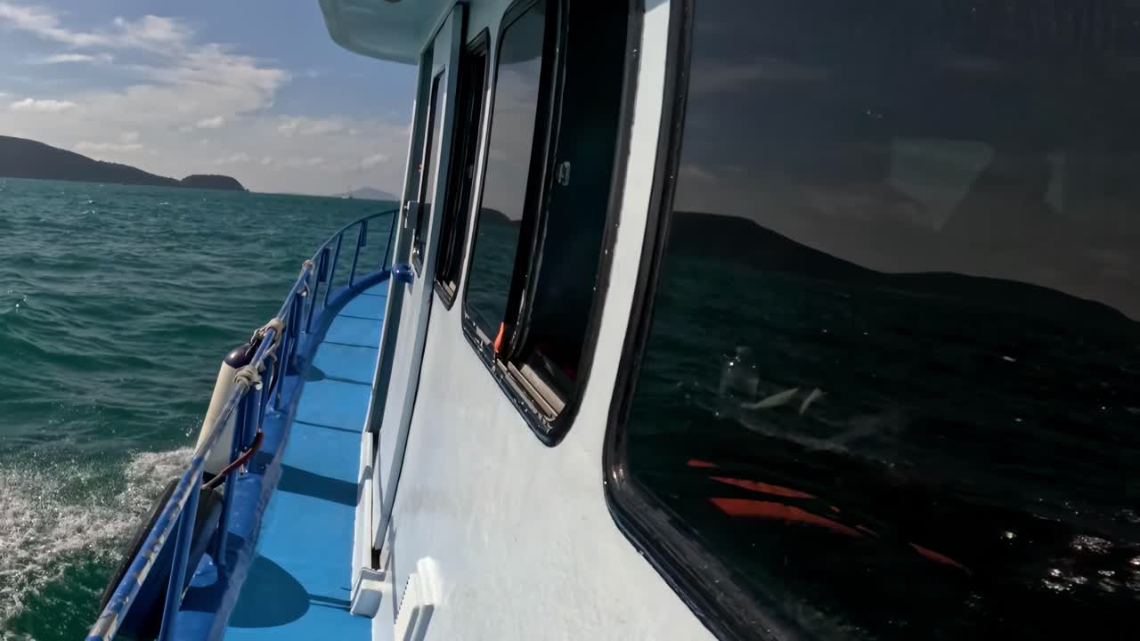 A close-up view of a boat deck with fishing rods, surrounded by green ocean waters and distant islands.